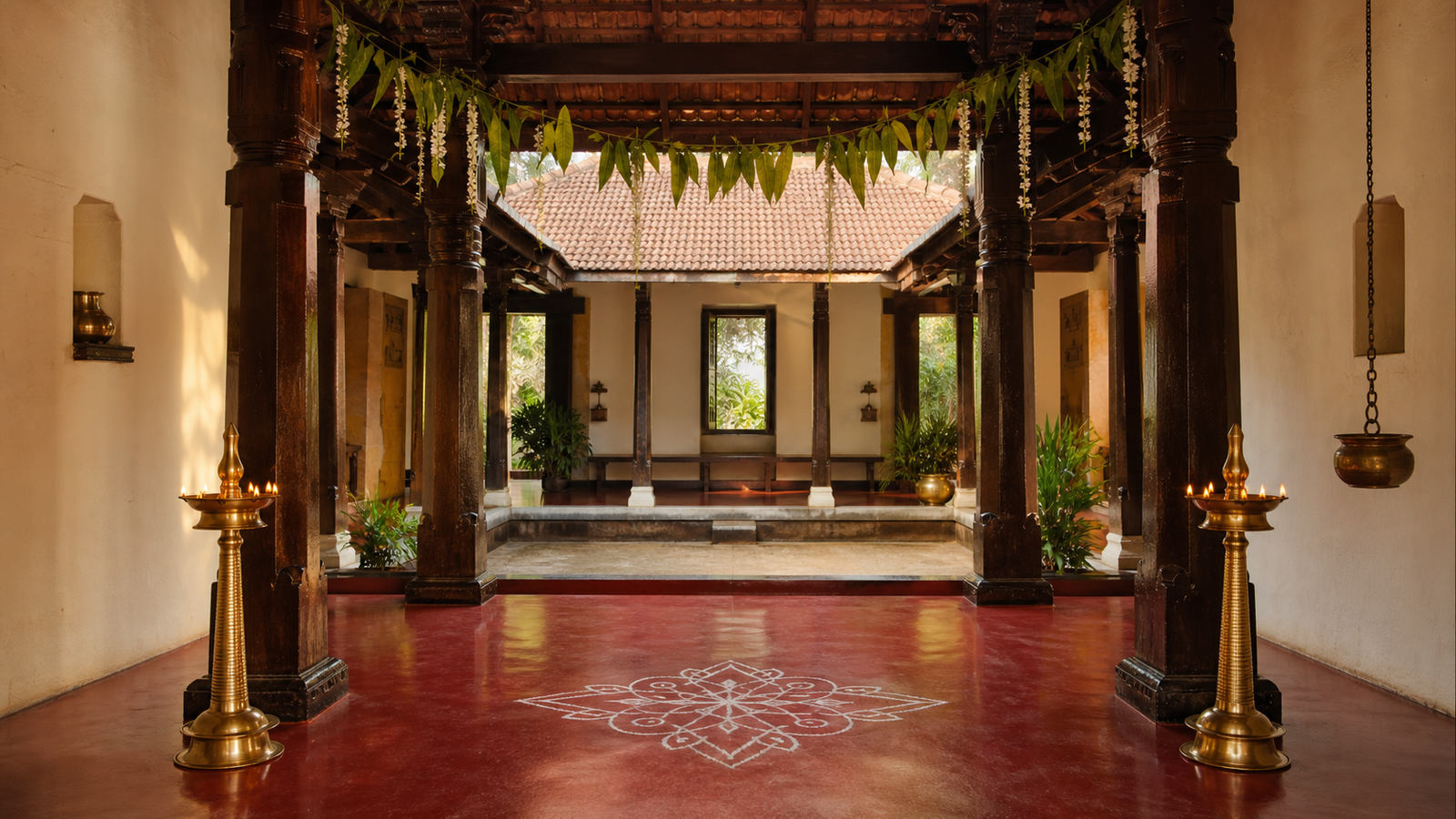 Traditional Kundapura-region courtyard with carved wood, red oxide floor, brass lamps and mango leaves